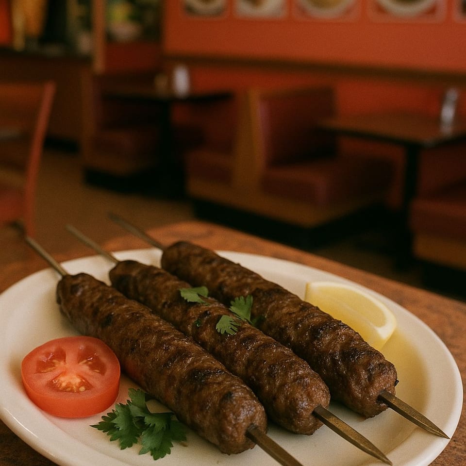 Three grilled Mediterranean kofta kebabs on a white plate with a lemon wedge and tomato slice.